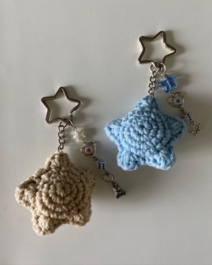 two crocheted keychains with star shaped objects attached to them on a white surface