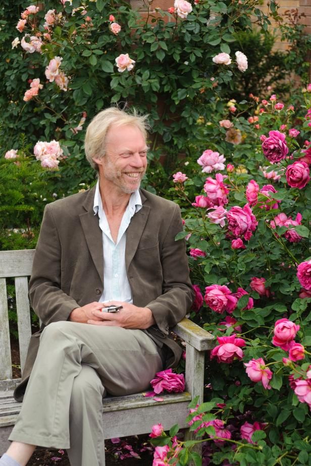 a man sitting on a bench in front of pink flowers and holding a cell phone