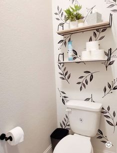 a white toilet sitting in a bathroom next to a wall with leaves painted on it