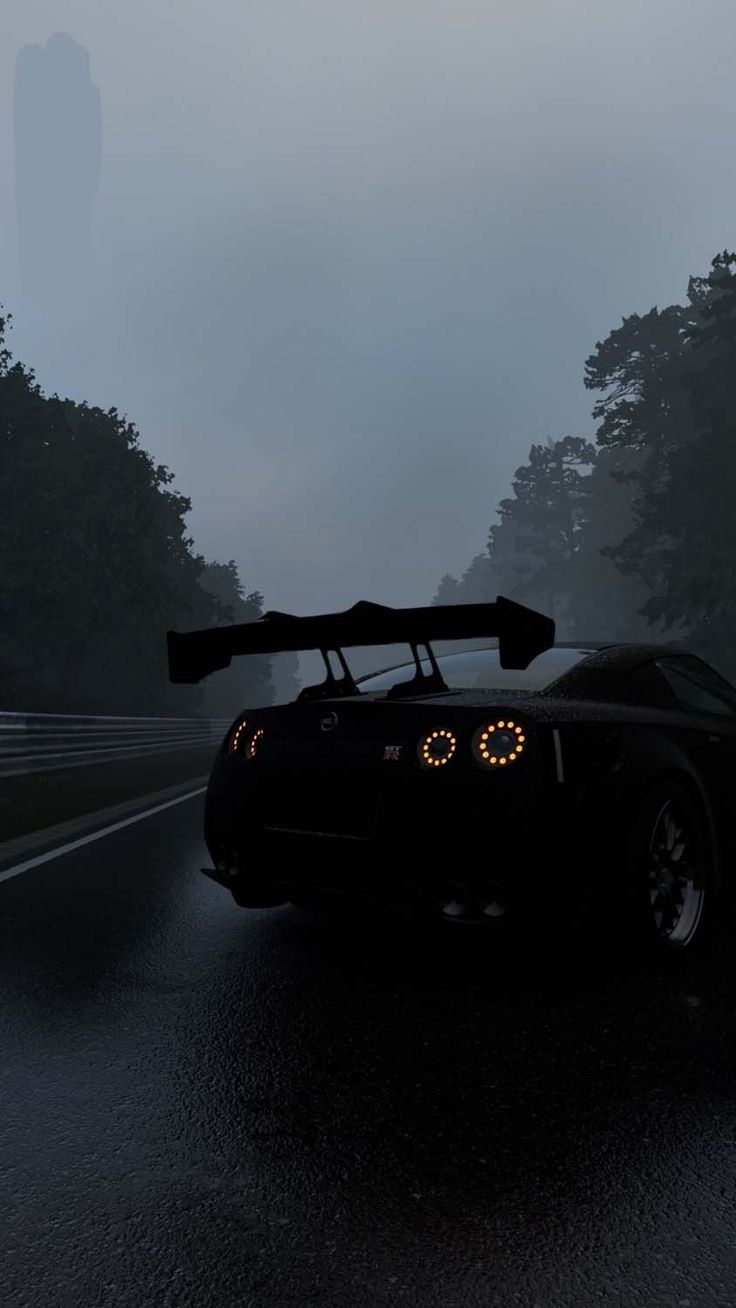 a black sports car driving down a wet road in the dark with its lights on