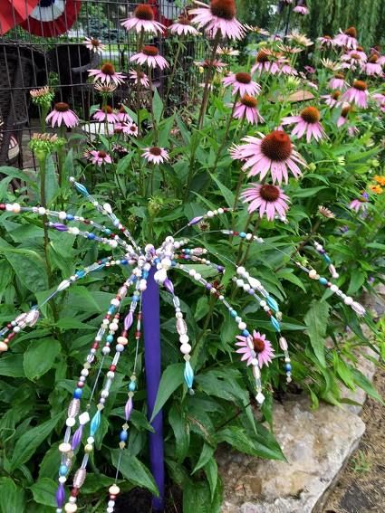 purple and white flowers in a garden next to a wire fence with blue ribbons on them