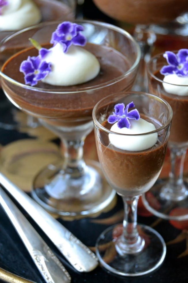 three desserts in glasses with purple flowers on the top and silverware next to them