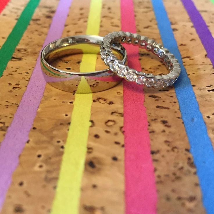 two wedding rings sitting on top of each other in front of colorful strips of paper