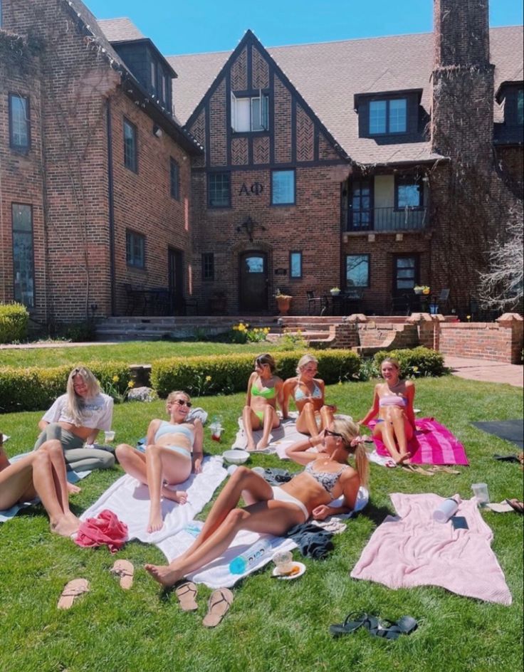 several women are sitting on the grass in front of a large brick building and eating