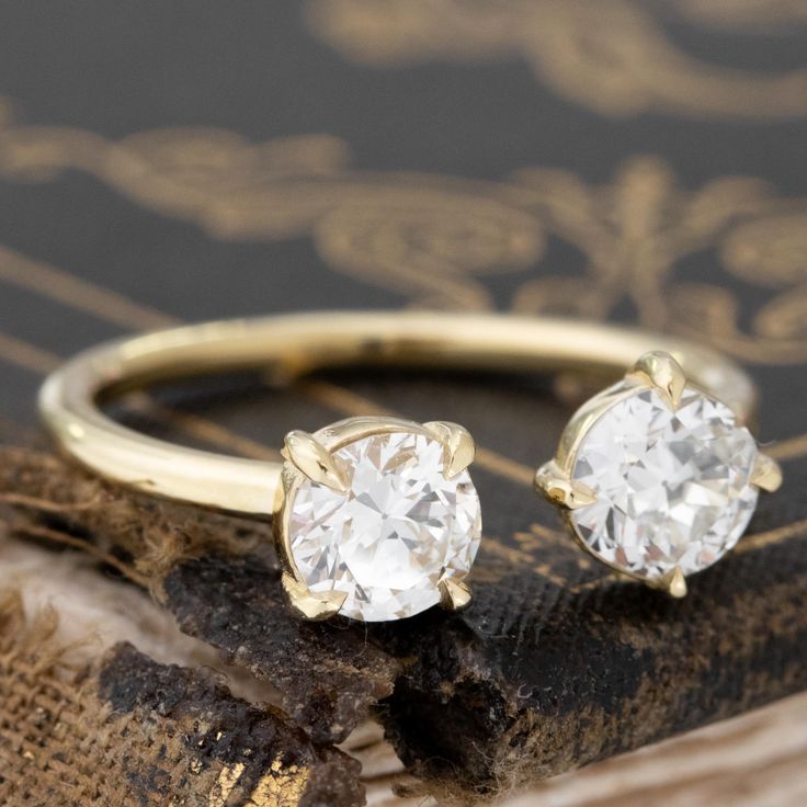 two engagement rings sitting on top of an old book with gold trimming and diamond accents