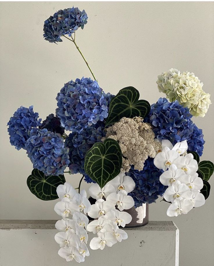 a vase filled with blue and white flowers on top of a table next to a wall