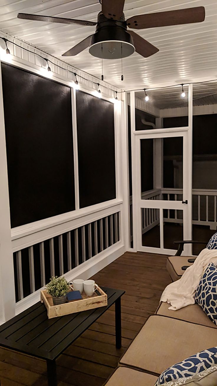 a living room filled with furniture and a fan on top of a wooden floor next to windows