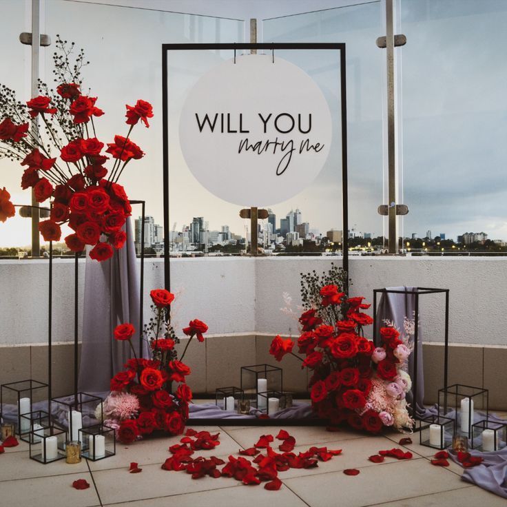 red flowers are on display in front of a sign that says will you marry me?