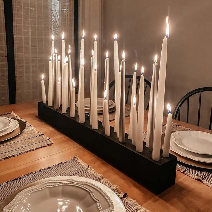 a long table with many lit candles on it and place settings in front of the candle holders