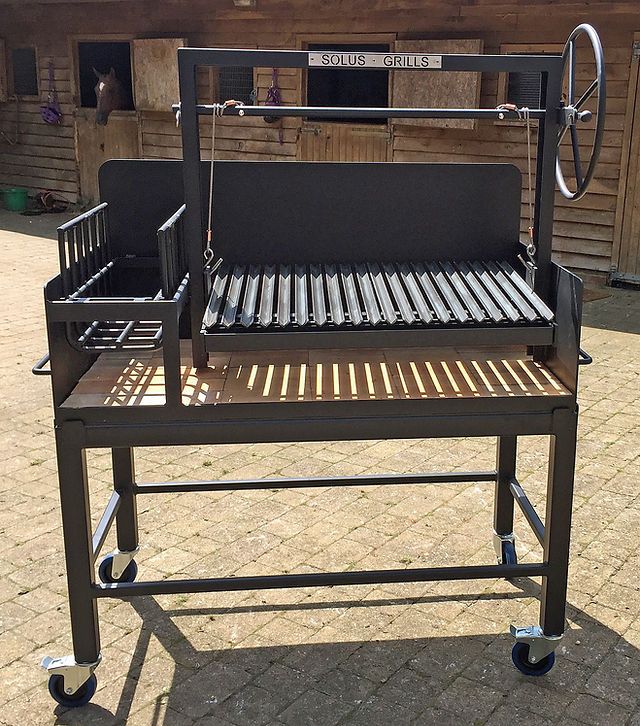 an outdoor grill sitting on top of a brick floor next to a building with wooden siding