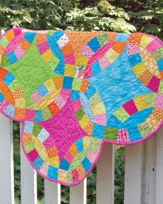 two colorful quilts are hanging on a white fence