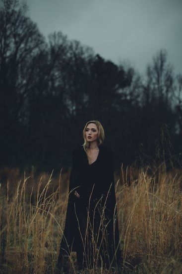 a woman standing in tall grass with trees in the background