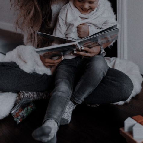 a woman sitting on the floor holding a baby and reading a book to her child