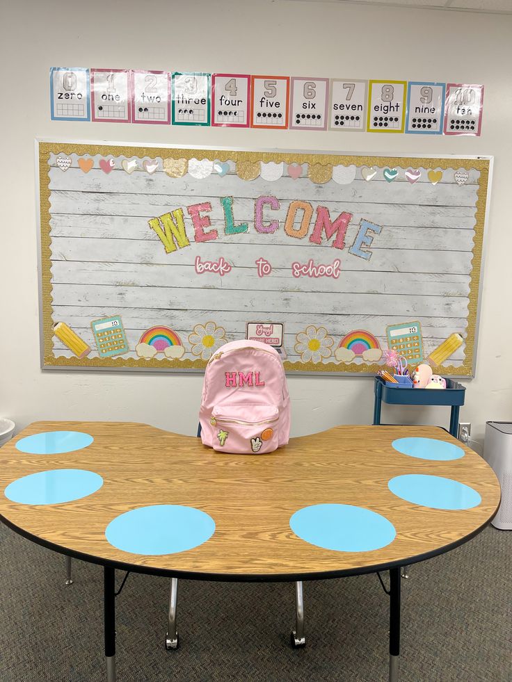 a wooden table topped with a pink backpack sitting in front of a welcome sign on the wall