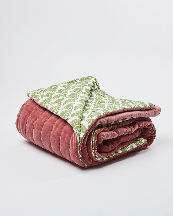 a pink blanket with green leaves is folded on a white surface and it's rolled up