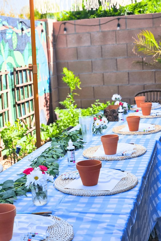 a long table with plates and cups on it in the middle of a garden area