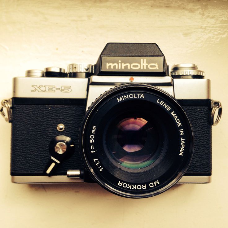 an old camera sitting on top of a white table next to a black and silver lens