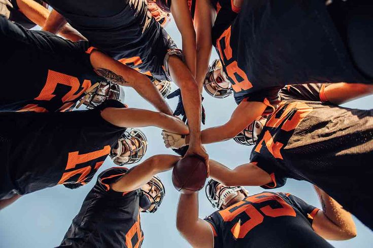 a group of football players standing in a huddle with their hands together stock photo