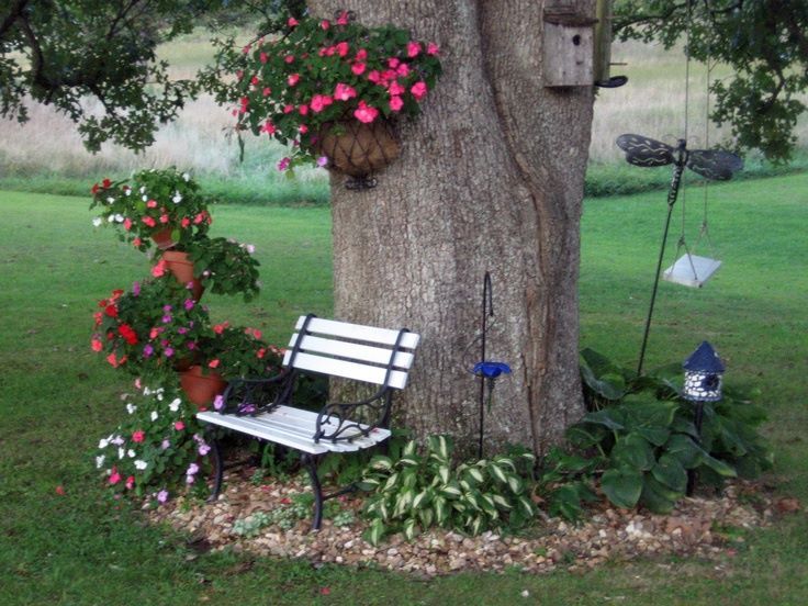 a white bench sitting under a tree next to a flower filled planter with flowers