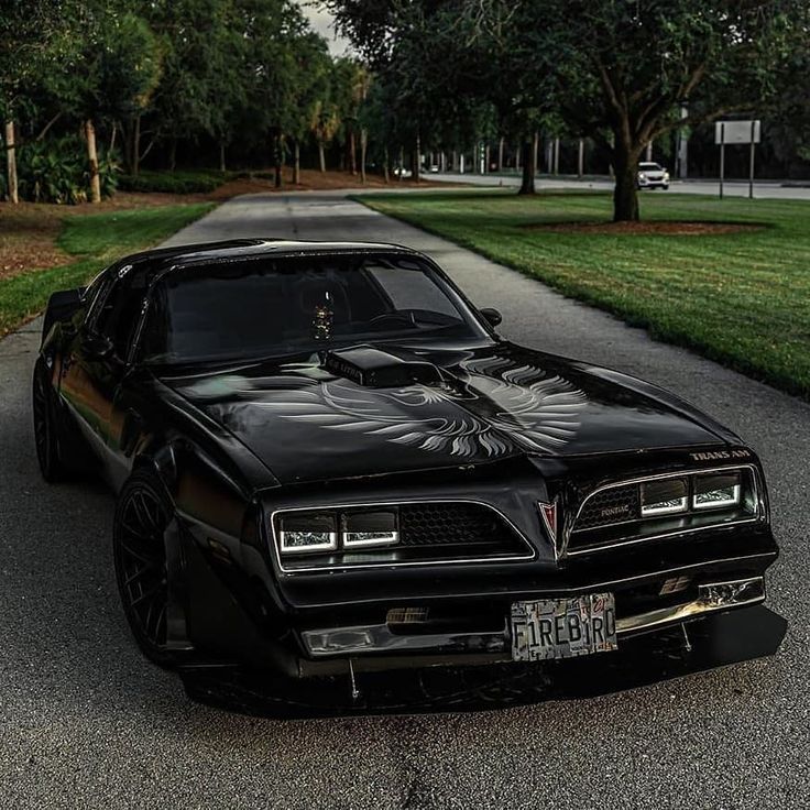 a black car parked on the side of a road next to some grass and trees