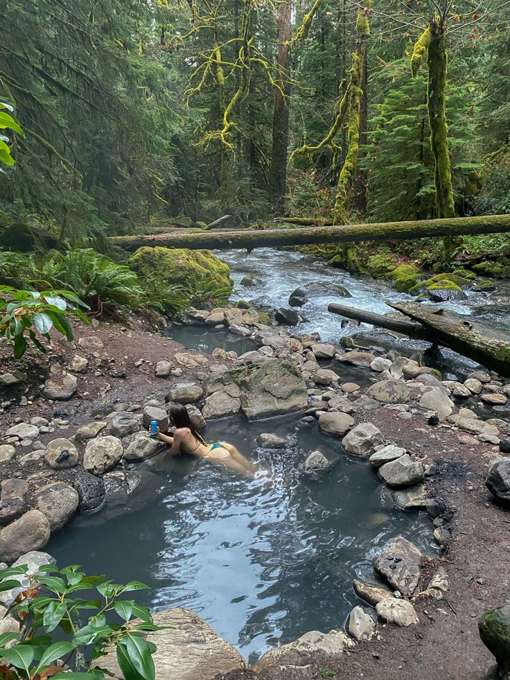 a person swimming in a river surrounded by rocks and green trees with moss growing on the ground