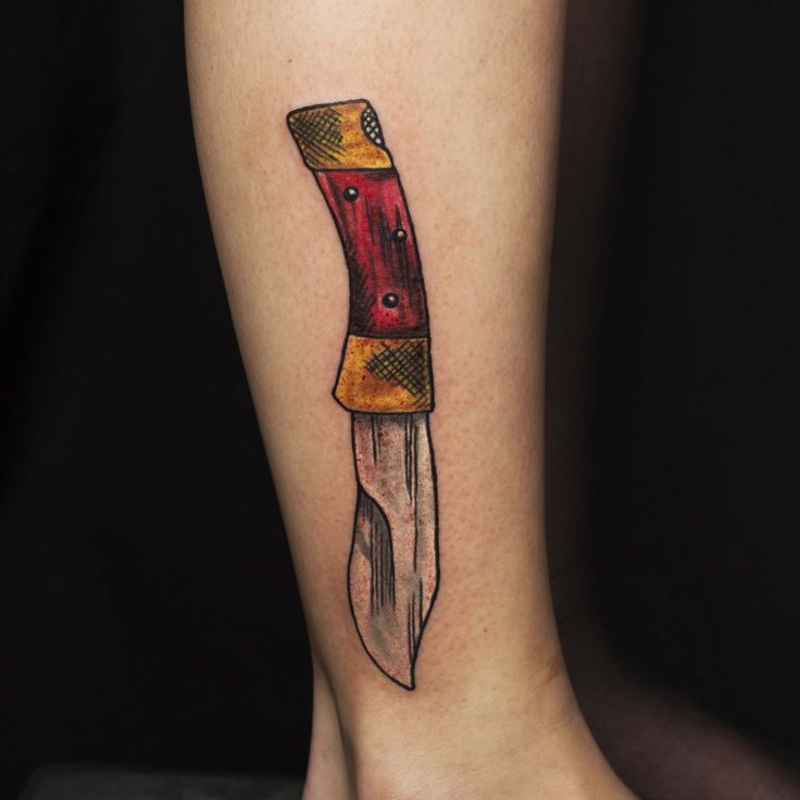 a knife tattoo on the leg of a woman's foot with an orange handle