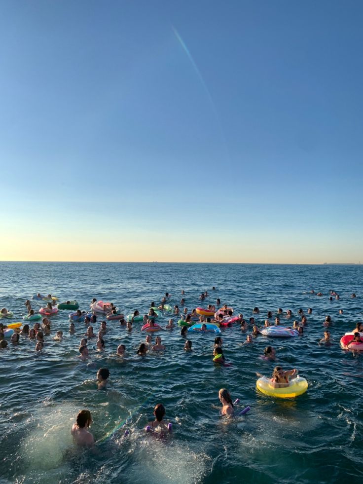 many people are swimming in the ocean on their rafts and floats, some with oars