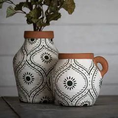 two white and brown vases with flowers in them on a wooden table next to a wall