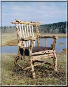 a wooden chair sitting on top of a grass covered field next to a lake with trees in the background