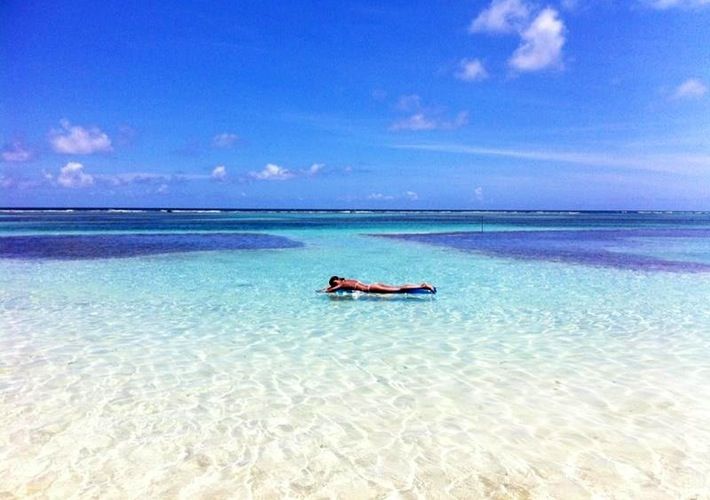 a person laying on their stomach in the water at an empty beach with clear blue skies