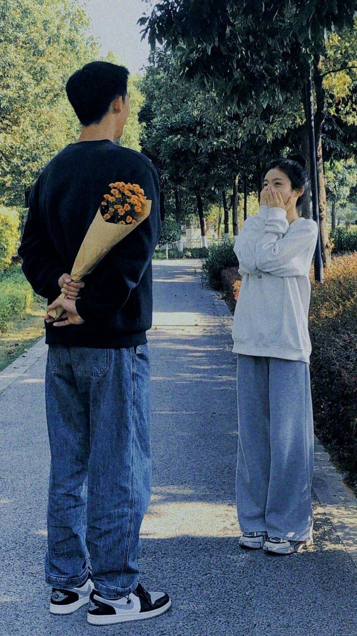 two people standing on the side of a road, one holding a flower and the other covering his face