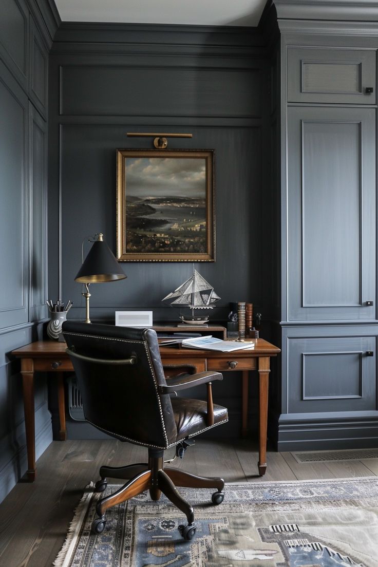 a home office with dark blue walls and wooden desk, leather chair, and painting on the wall