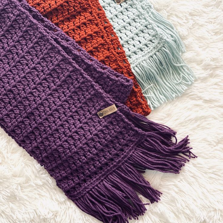 three different colors of knitted scarves laying on a white furnishing area