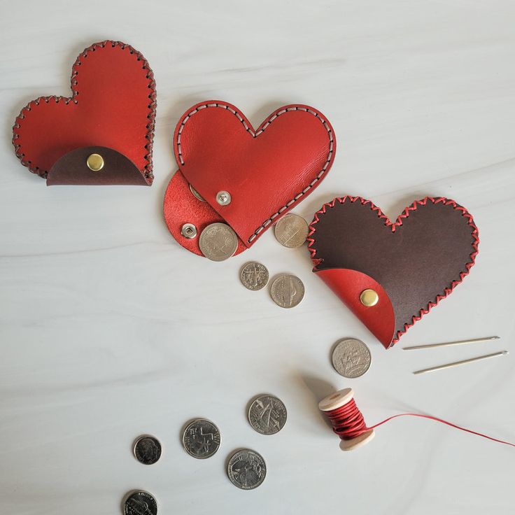 two heart shaped leather purses next to some coins and thread on a white surface