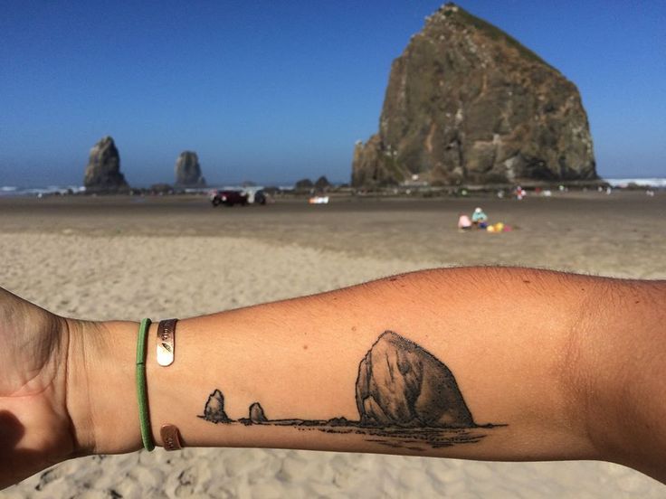 a person's arm with a rock on the beach in front of some rocks