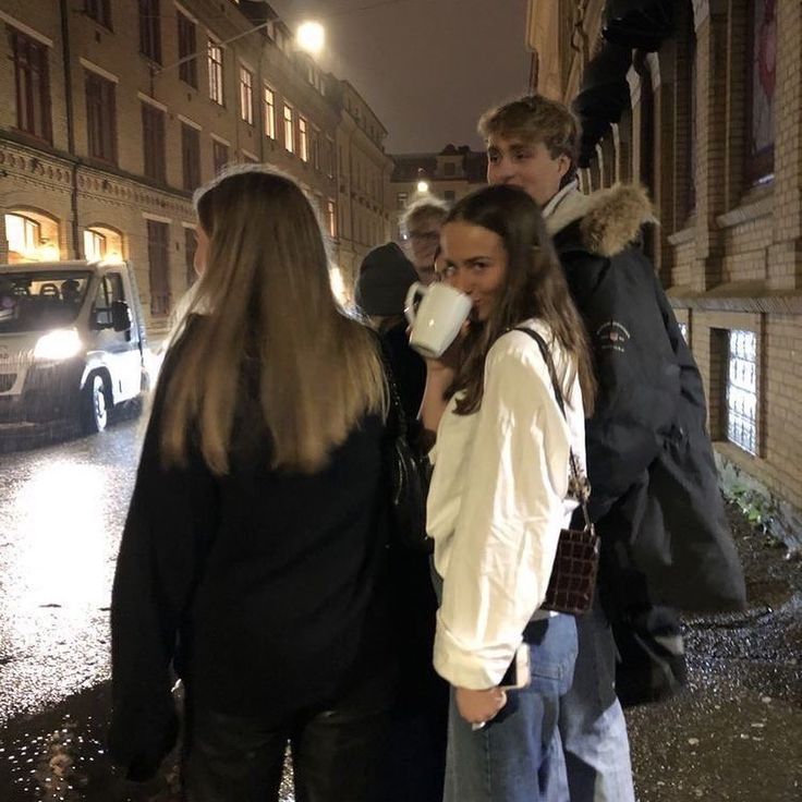 group of people standing on the side walk drinking from paper cups in front of them