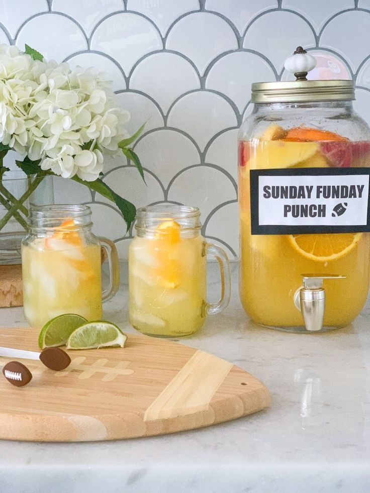 some drinks are sitting on a counter next to a cutting board and vase with flowers