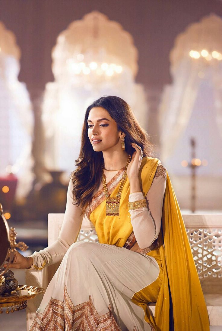 a woman sitting on top of a white bench wearing a yellow and beige dress with gold accents