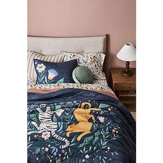 a bed with a blue comforter and pillows on top of it next to a lamp