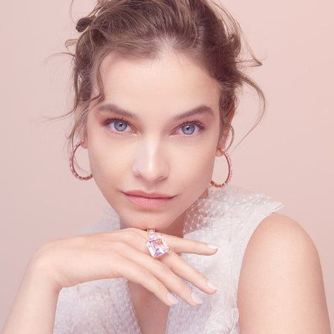 a woman with blue eyes wearing a white top and gold hoop earrings is posing for the camera