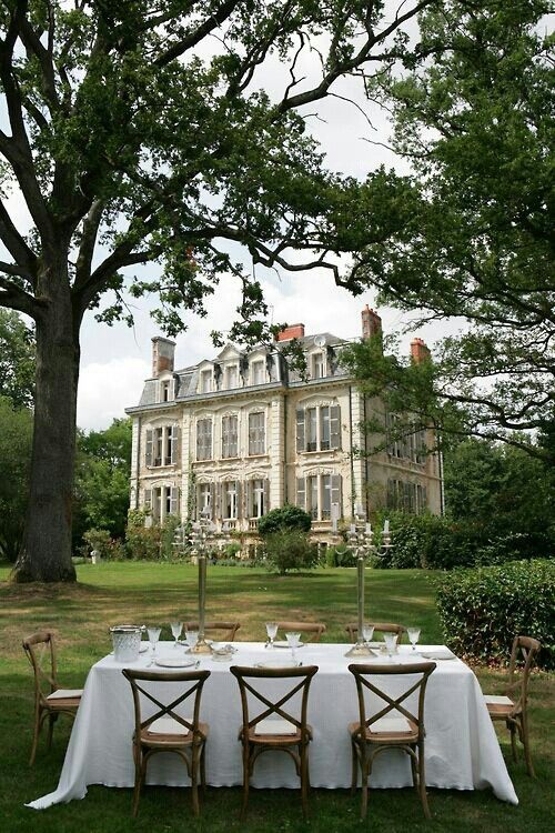 an image of a table and chairs in front of a large house with trees on the lawn