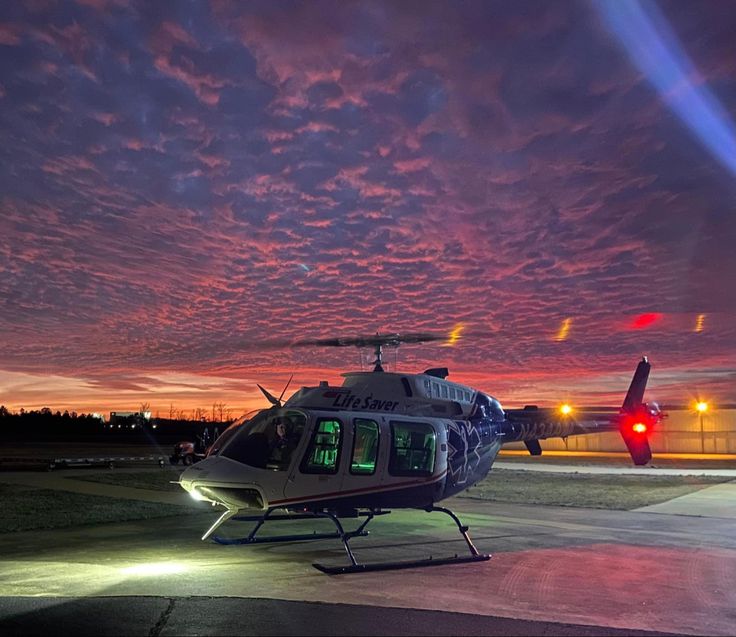 a helicopter sitting on top of an airport tarmac at night with the sun setting