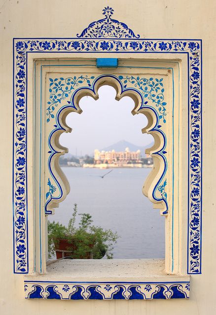 an ornate window with blue and white paint on the side of a building next to water