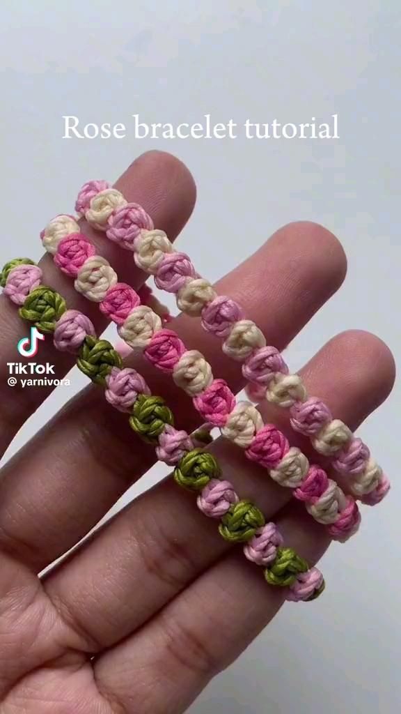 a hand is holding three crocheted bracelets in pink, green and white