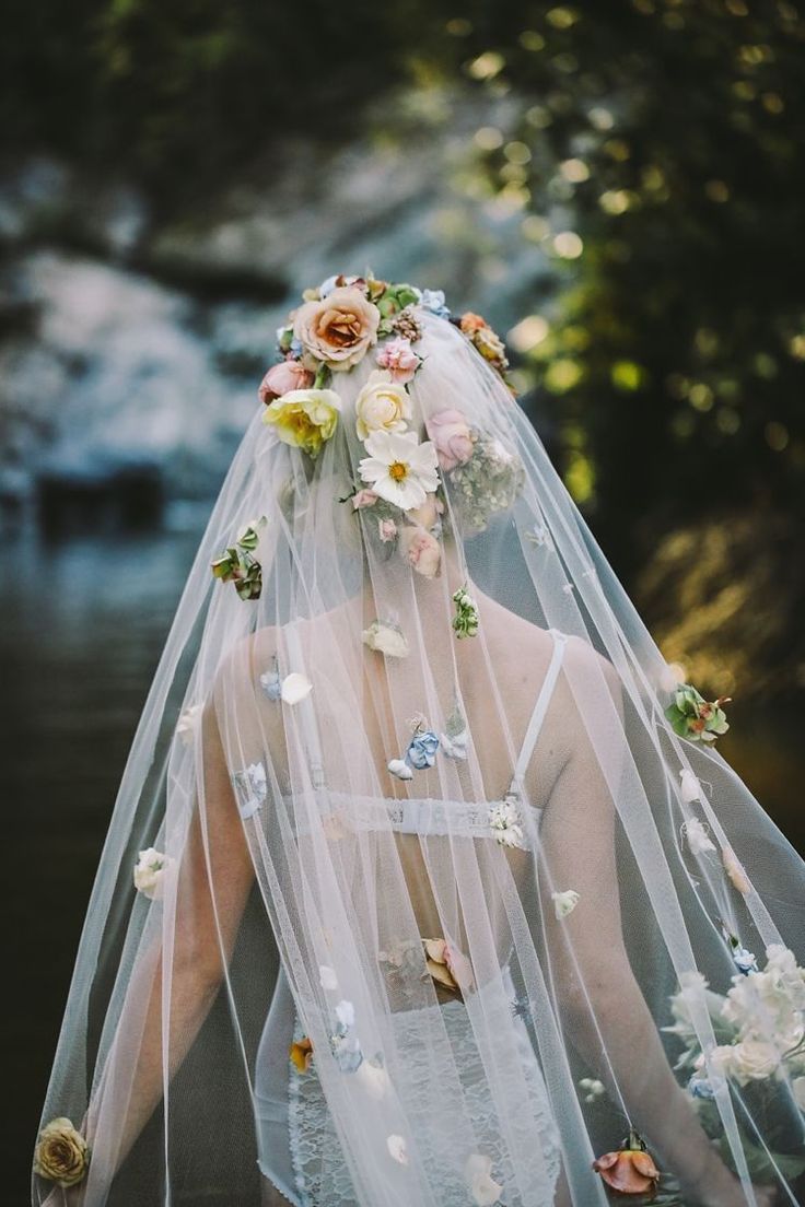 a woman wearing a veil with flowers on her head is standing in front of a stream