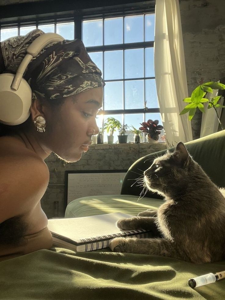 a woman with headphones on laying next to a cat and looking at her laptop