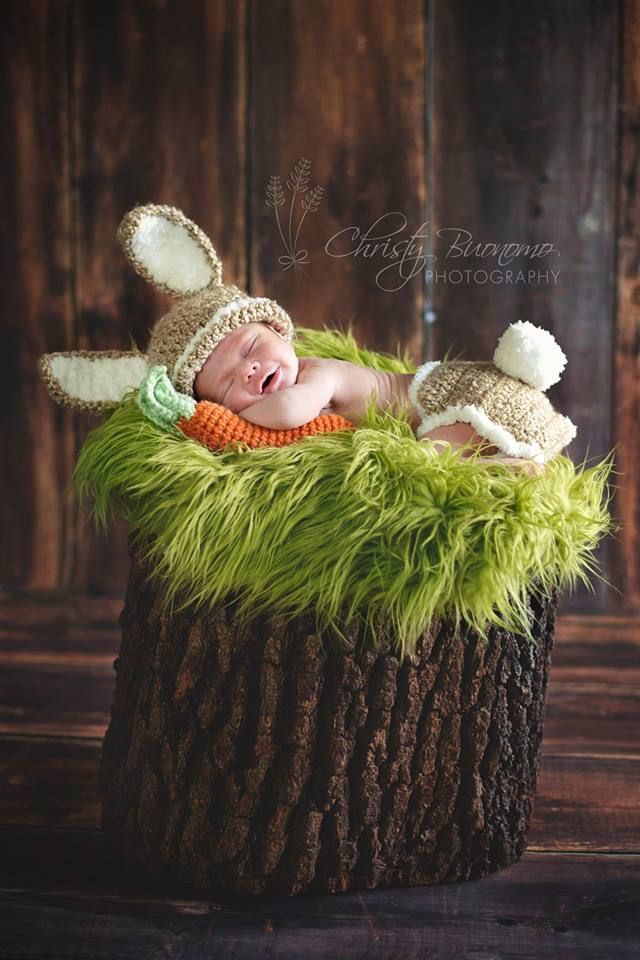 a baby is sleeping in a tree stump wearing a bunny hat and green fuzzy pants