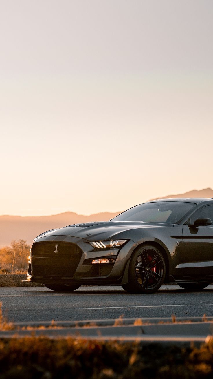 a black sports car is parked on the side of the road with mountains in the background