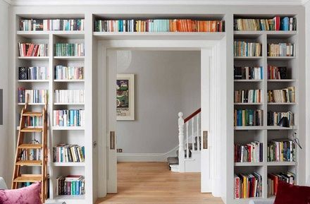 a living room filled with lots of white furniture and bookshelves full of books