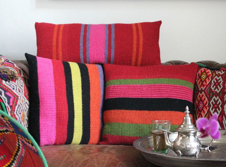 the colorful pillows are on the couch by the tray with silver teapots and cups